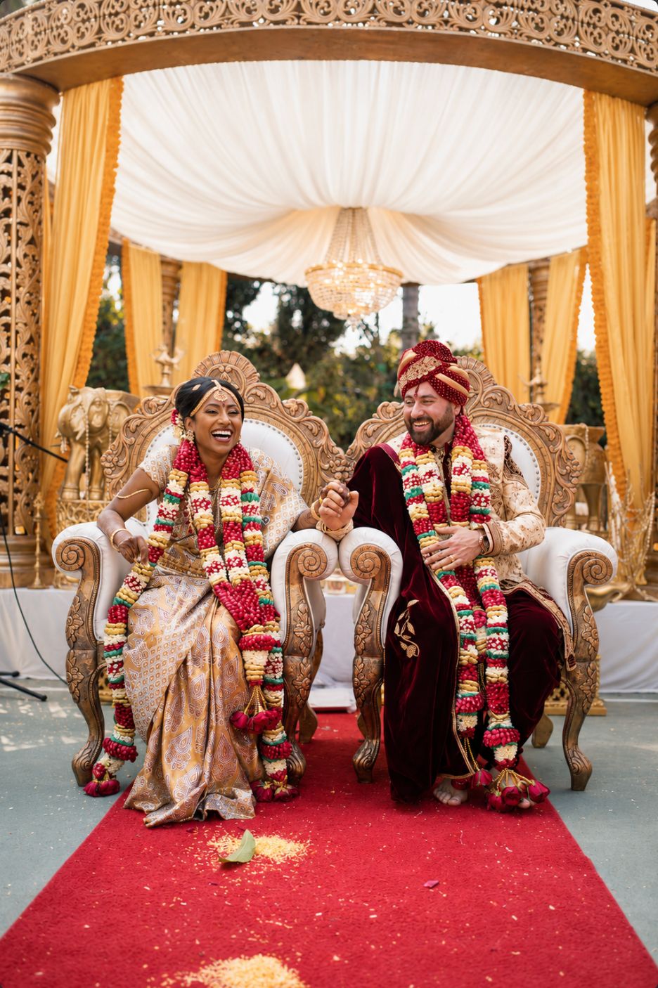 Bride and groom laughing on ornate thrones under a gold mandap at a traditional Indian wedding ceremony in Southern California, photographed by Murrieta Media